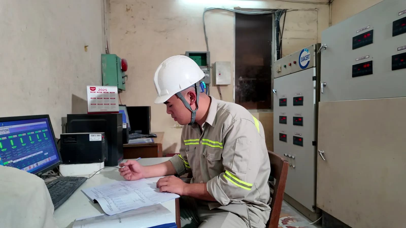 Vận hành viên đội mũ bảo hộ theo dõi hệ thống trong phòng điều khiển nhà máy