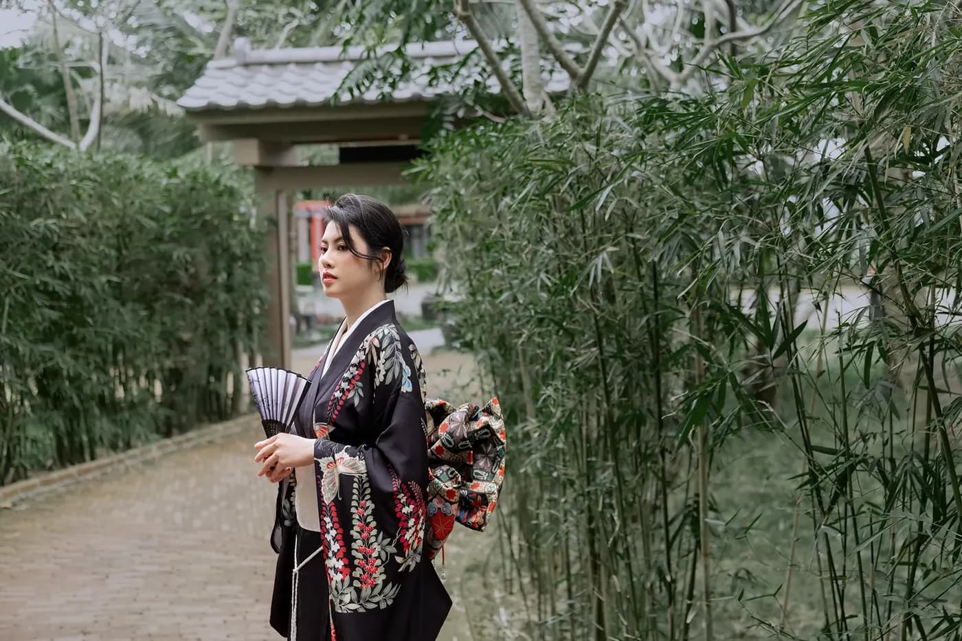 A model in a kimono holding a fan on a bamboo-lined path, Mikazuki